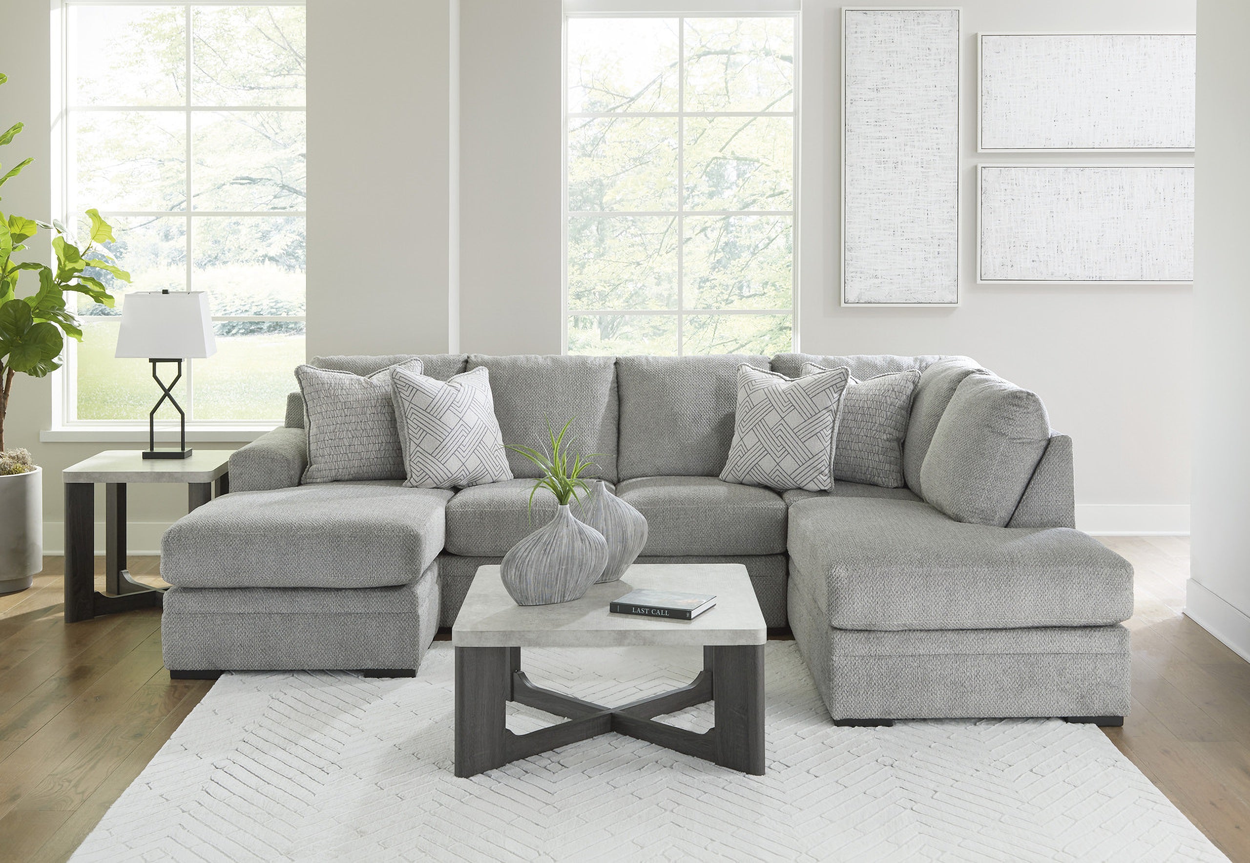 Grey plush U-shaped sectional sofa with chaise, Ashley Casselbury 2-piece design in cement fabric, shown in a living room setting.