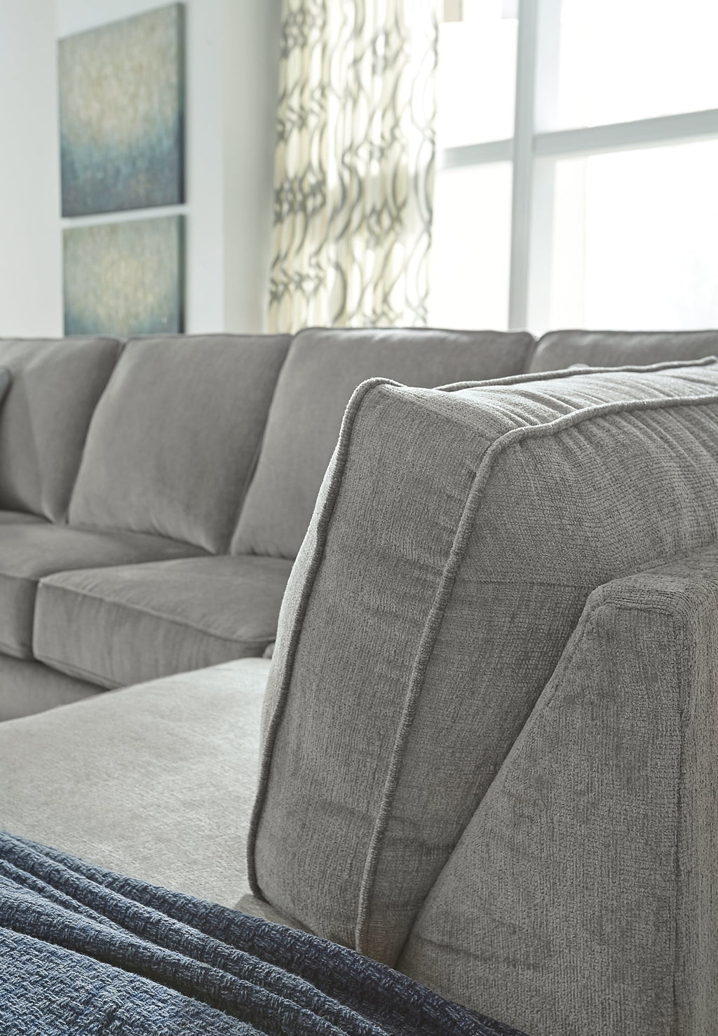 Grey L-shaped sleeper sectional by Ashley with plush cushions and modern design, shown in a stylish studio setting.